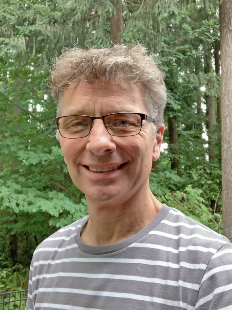 Matthew Shepherd with a gray and white t-shirt, glasses and a big smile