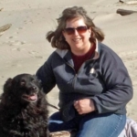 Linda poses on the beach with a shaggy black dog.