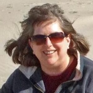 Linda poses on the beach with a shaggy black dog.