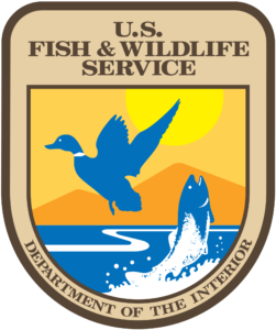 a tan badge with an image of a bird and fish, a sun and mountain and water.