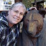 Susan smiles and leans her head against a carved wooden bear.