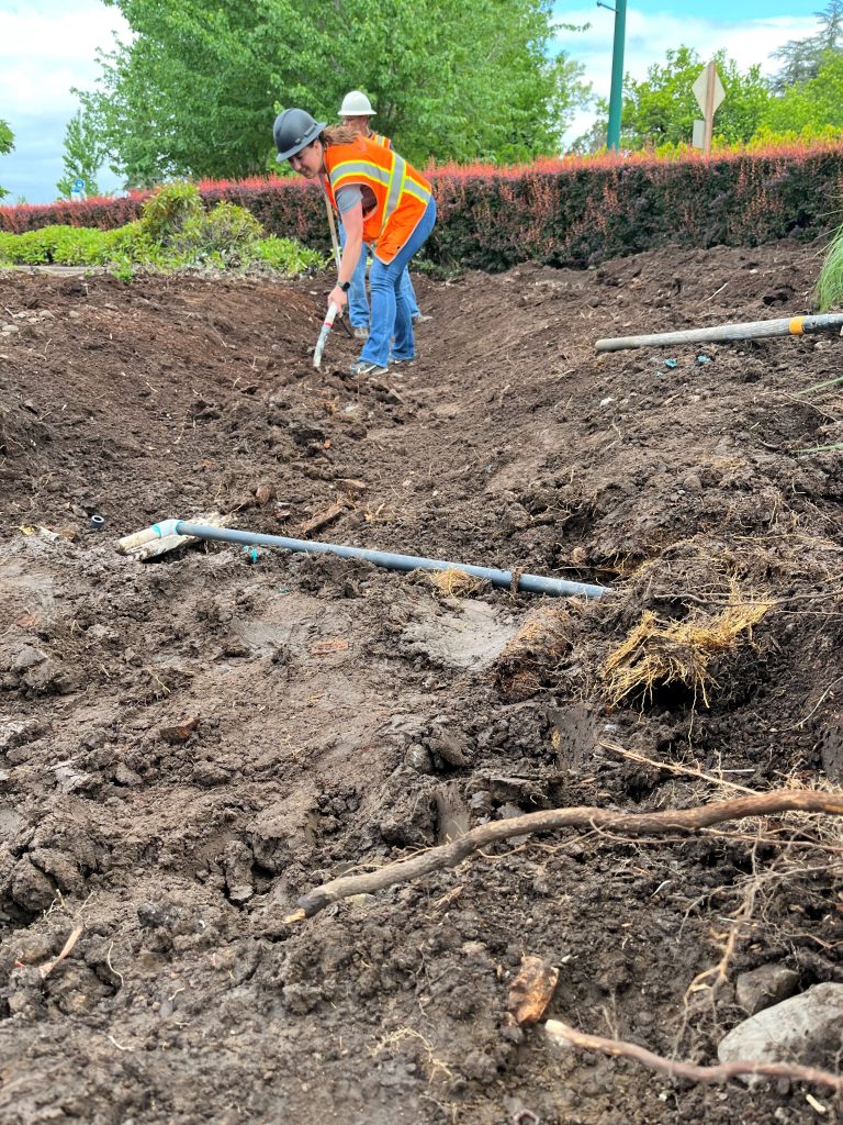 A city worker shaping the excavated basin with a shovel.