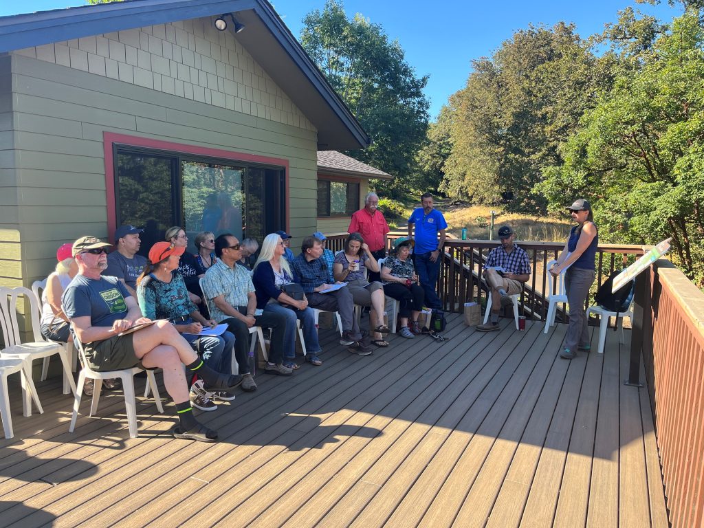 People sitting on an outdoor porch listening to a presenter at the workshop.