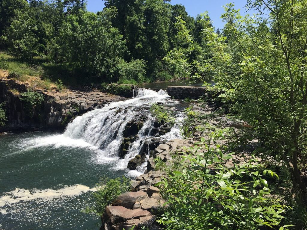 a natural waterfall with a concrete dam above it. The dam has been breached and is crumbling.