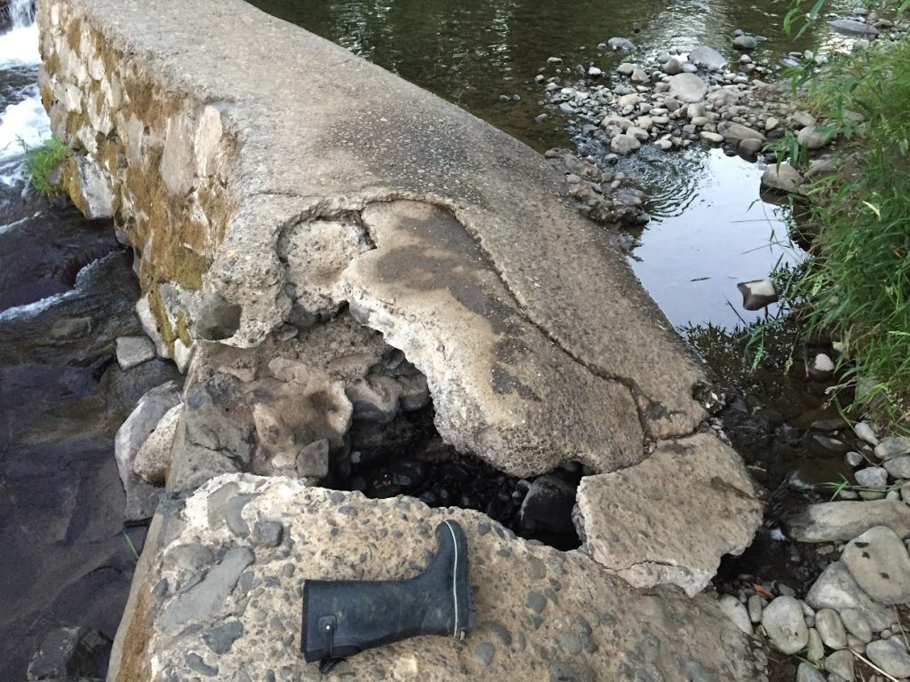 A close up of the crumbling concrete of the Scotts Mills Dam with a rubber boot for scale showing that the cracks are larger than the boot.