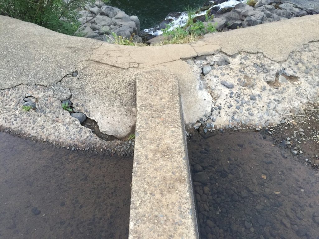 A close up of the Scotts Mills Dam where a concrete wall intersects the dam and on both sides of the wall the concrete is crumbling.