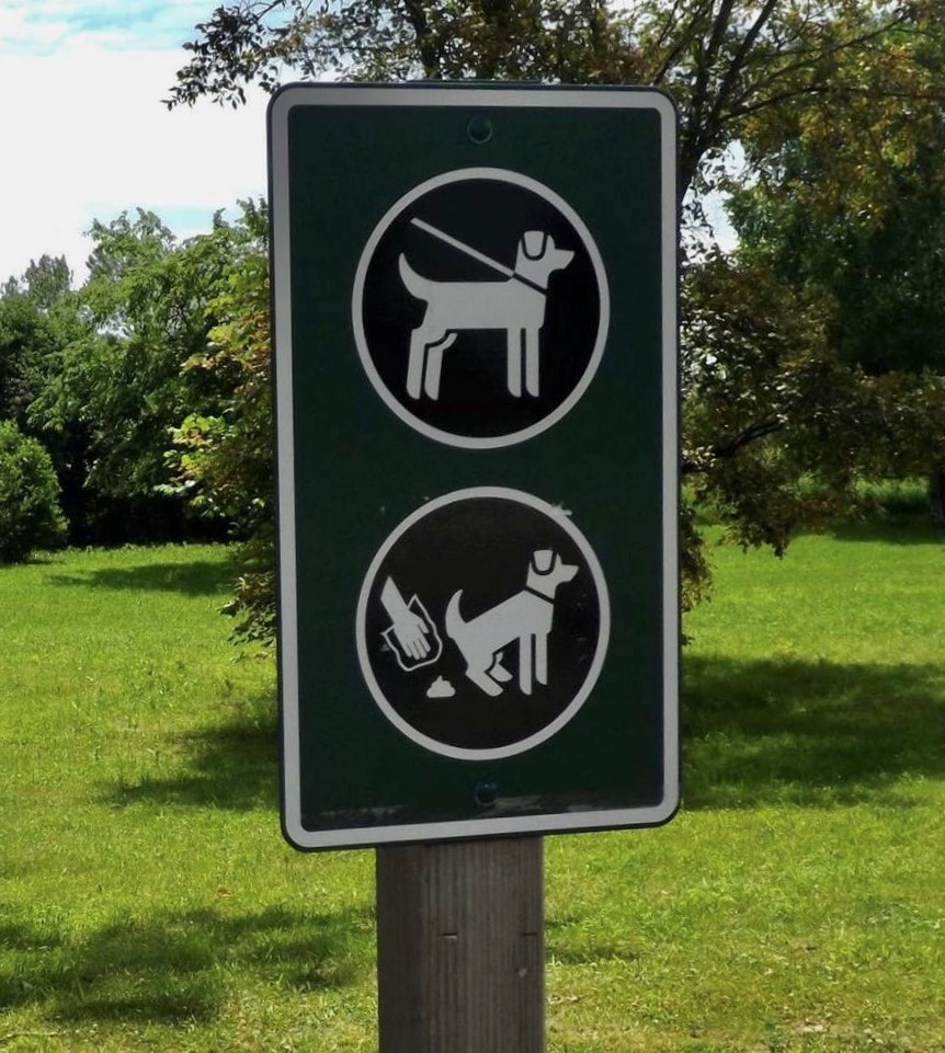 a dog sign at a park showing a dog on leash and a hand picking up dog waste