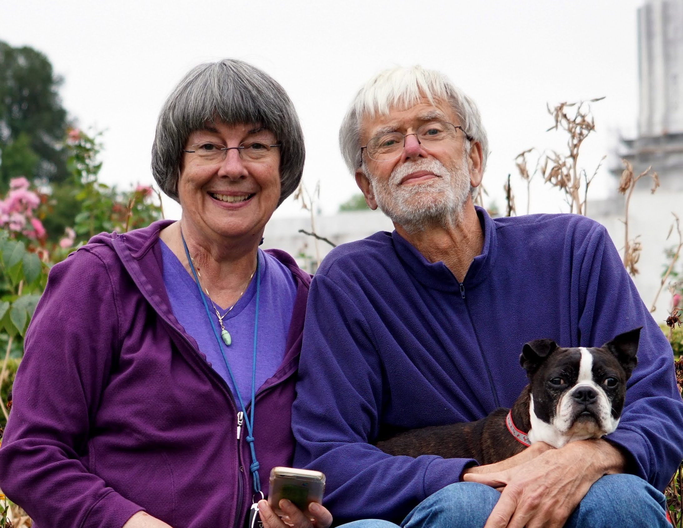 a photo of Stephanie and Ray and their little black and white dog sitting on a garden bed edge outside the capital building in Salem, OR.